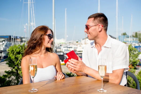 Pareja sonriente con champán y regalo en la cafetería —  Fotos de Stock