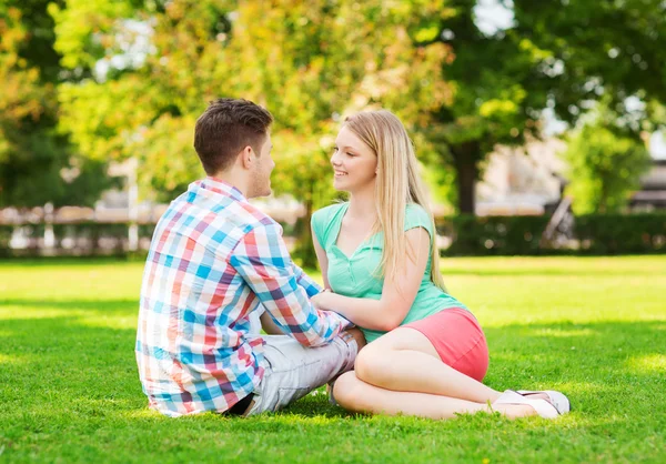 Couple souriant assis sur l'herbe dans le parc — Photo