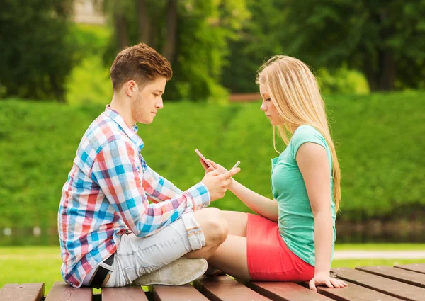 Pareja con smartphones sentados en el banco en el parque — Foto de Stock