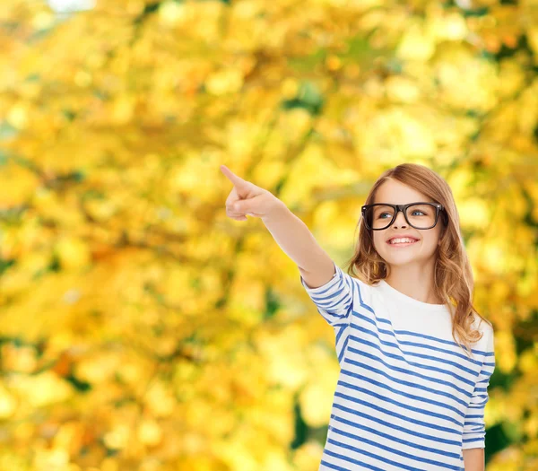 Cute little girl in eyeglasses pointing in the air — Stock Photo, Image