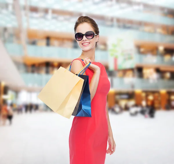 Mujer sonriente en vestido rojo con bolsas de compras — Foto de Stock