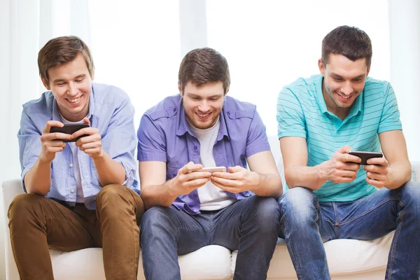 Amigos sonrientes con teléfonos inteligentes en casa —  Fotos de Stock