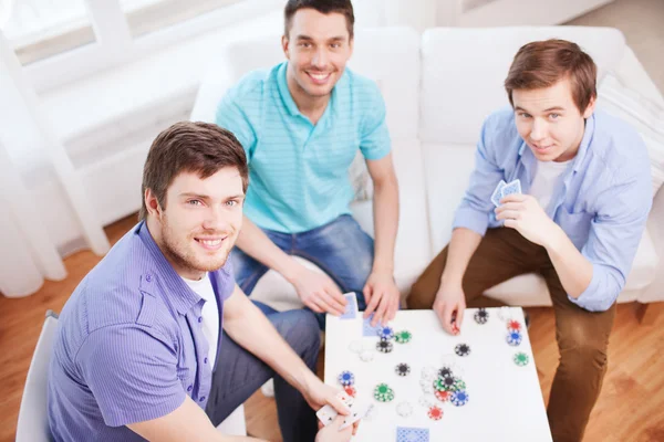 Três sorridentes amigos do sexo masculino jogando cartas em casa — Fotografia de Stock