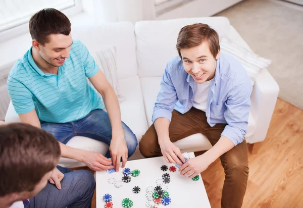Τρεις χαμογελώντας αρσενικούς φίλους παίζοντας χαρτιά στο σπίτι — Φωτογραφία Αρχείου