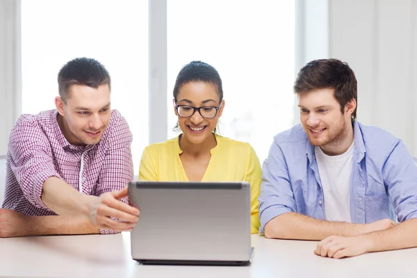 Трое улыбающихся коллег с ноутбуком в офисе — стоковое фото