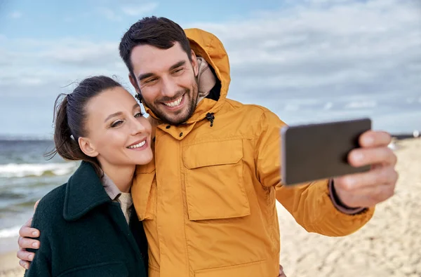 Пара со смартфоном на осеннем пляже — стоковое фото