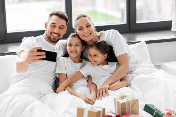 Familj med julklappar tar selfie i sängen — Stockfoto