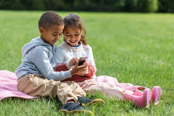 Kids with smartphone sitting on blanket at park — Stock Photo, Image