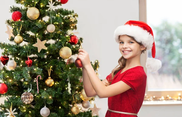 Glad tjej i santa hatt dekorera julgran — Stockfoto