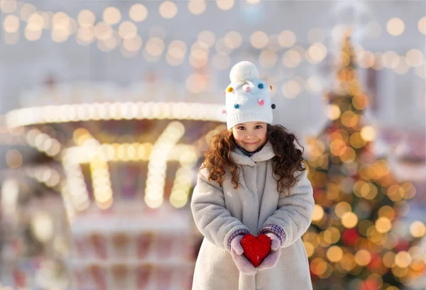 Happy little girl with heart over christmas lights — Stock Photo, Image
