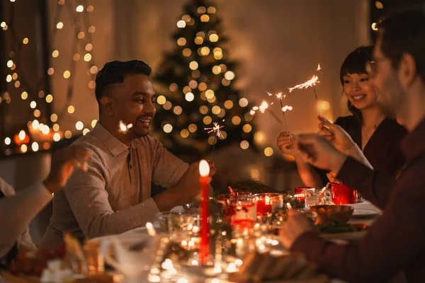 Amigos felizes com faíscas no jantar de Natal — Fotografia de Stock