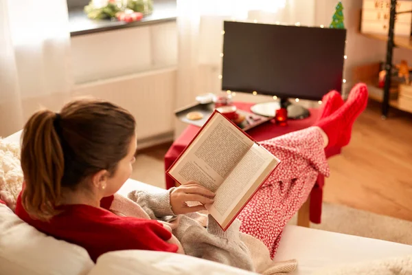 크리스마스에 집에서 책을 읽는 젊은 여자 — 스톡 사진