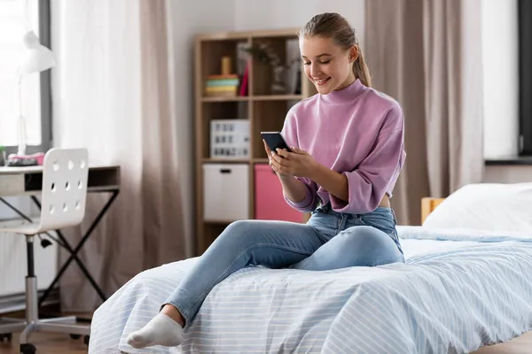 Boldog lány okostelefonnal ül az ágyon otthon — Stock Fotó