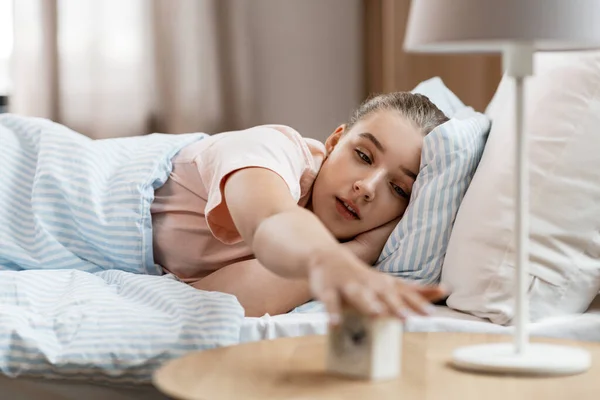 Chica soñolienta con despertador despertando en la cama — Foto de Stock