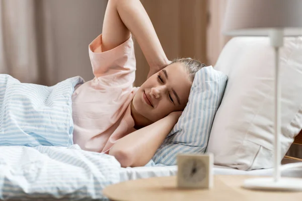 Slaperig meisje met wekker ontwaken in bed — Stockfoto