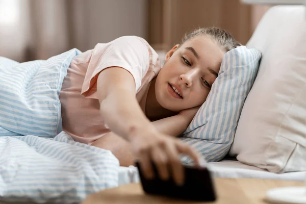 Девушка выбирает смартфон из кровати стол дома — стоковое фото