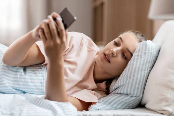 Šťastná dívka s chytrým telefonem v posteli doma — Stock fotografie