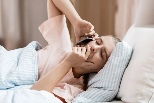 sleepy girl calling on smartphone in bed at home