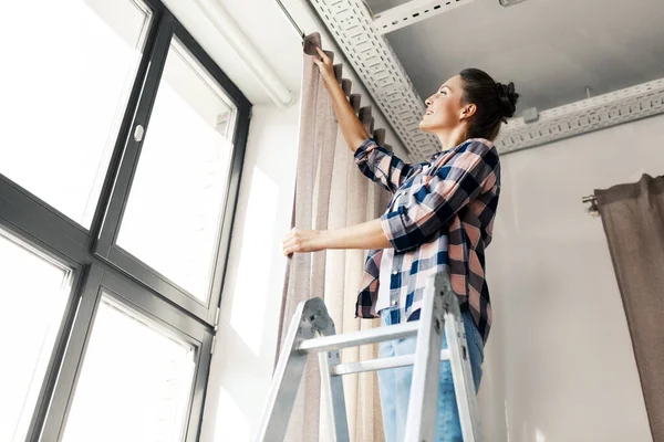 Mujer en escalera colgando cortinas en casa —  Fotos de Stock