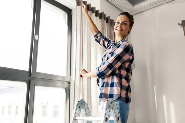 Woman on ladder hanging curtains at home — Stock Photo, Image