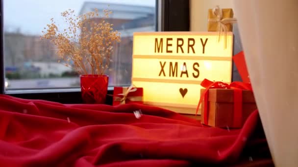 Счастливого Рождества на светлой коробке и подарков на окне — стоковое видео