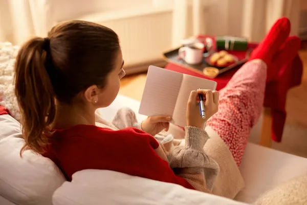 Mujer escribiendo a cuaderno en casa en Navidad — Foto de Stock