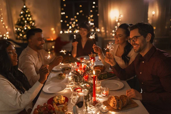 Šťastní přátelé s jiskry na vánoční večeři — Stock fotografie