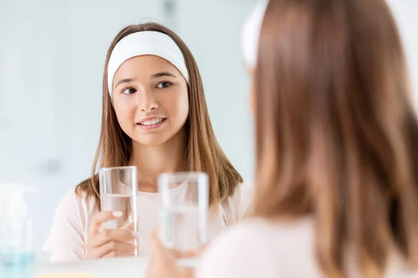 Tonårstjej med glas vatten tittar i spegeln — Stockfoto