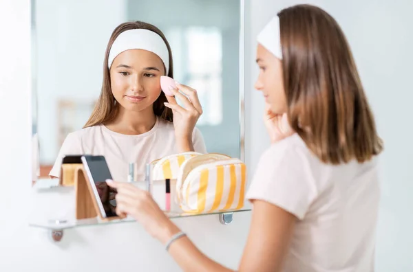 Adolescente con teléfono inteligente utilizando maquillaje esponja — Foto de Stock