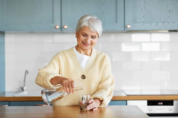Šťastná žena s džbánem vody na kuchyni doma — Stock fotografie