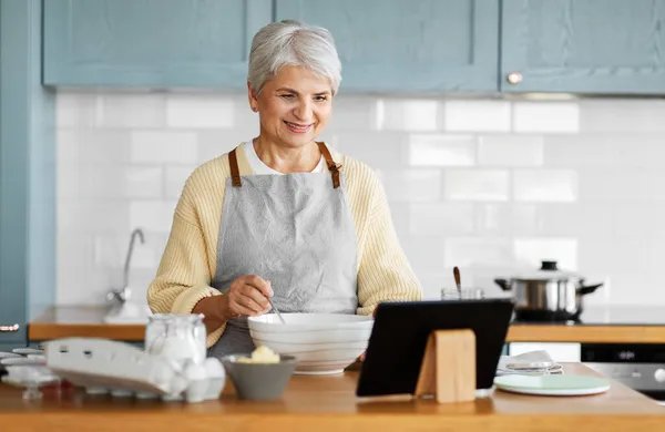 Kvinna med tablett dator matlagning mat på kök — Stockfoto