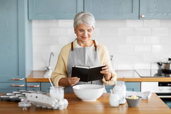 Boldog nő szakács könyv főzés élelmiszer a konyhában — Stock Fotó