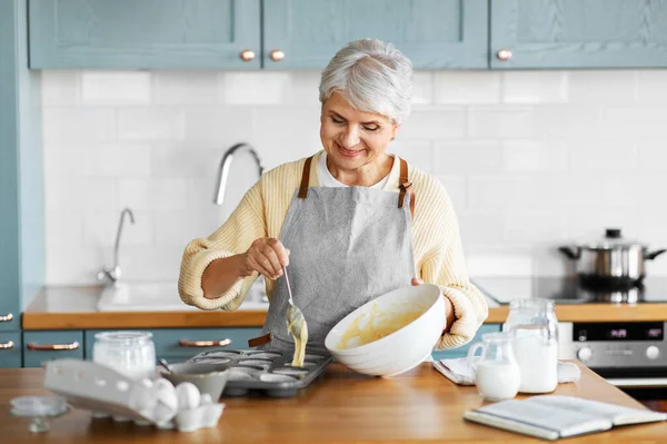 Kvinna sätta smet i bakning formar på kök — Stockfoto