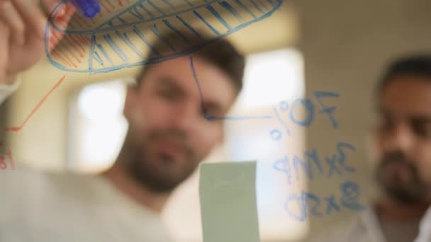 Мужчины, работающие в офисе с графиками на стеклянной доске — стоковое видео