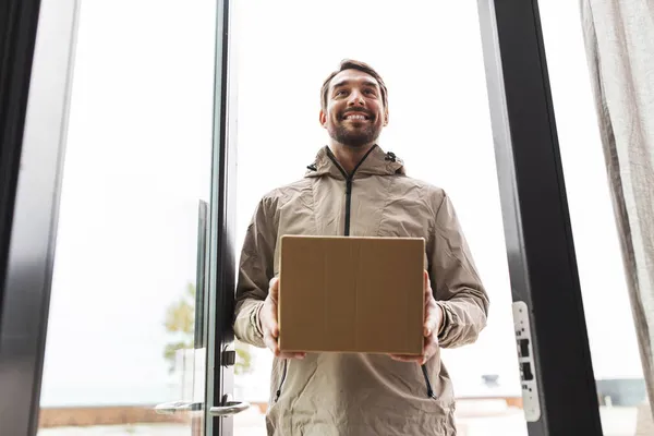 Repartidor sonriente con caja de paquetes a puerta abierta —  Fotos de Stock