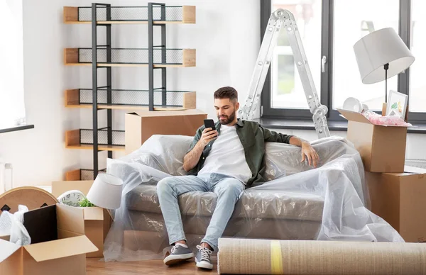 Hombre con teléfono inteligente y cajas que se mudan a un nuevo hogar —  Fotos de Stock