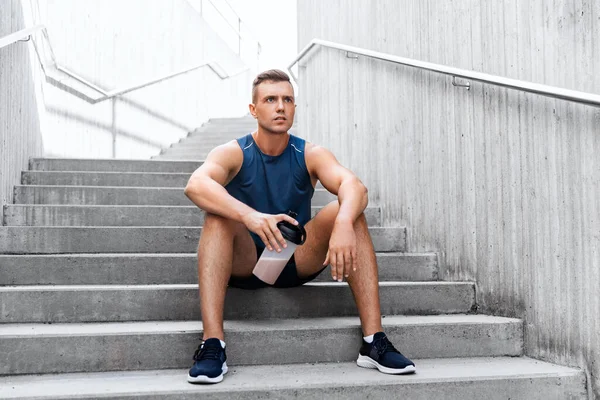 Sportsman with shake in bottle sitting on stairs — Stock Photo, Image