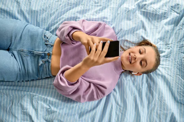 Chica en auriculares con teléfono inteligente acostado en la cama — Foto de Stock