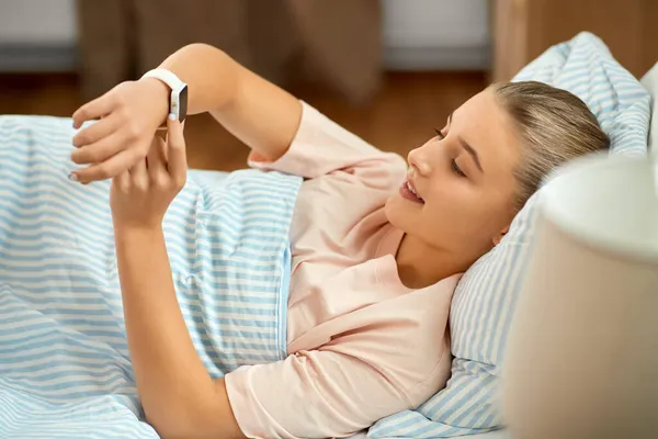 Chica sonriente con reloj inteligente acostado en la cama en casa —  Fotos de Stock