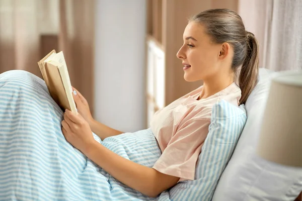 Sorridente ragazza lettura libro a letto a casa — Foto Stock