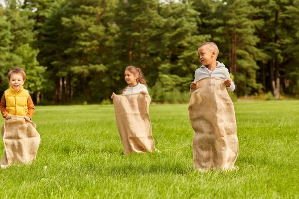 Niños felices jugando juego de saltos bolsa en el parque — Foto de Stock