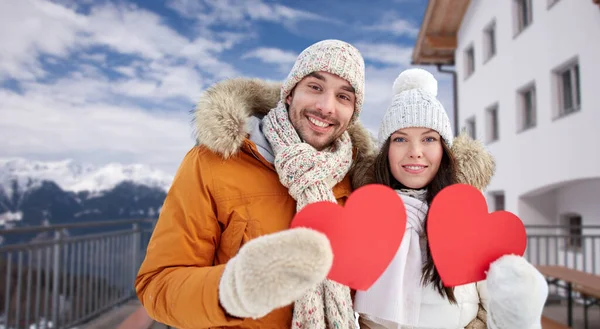 Casal feliz com corações vermelhos sobre resort de inverno — Fotografia de Stock