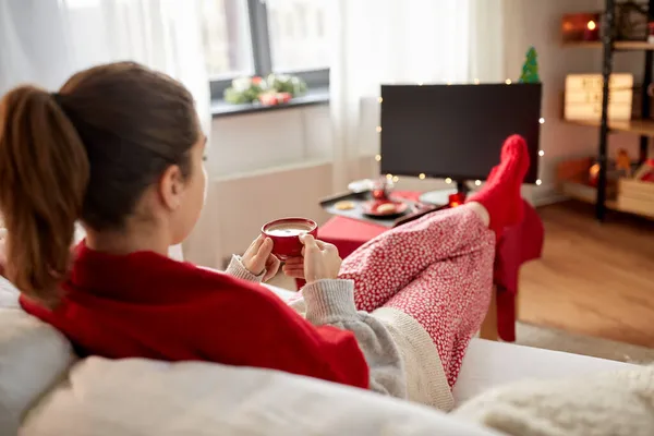 Kvinna tittar på tv och dricker kaffe på jul — Stockfoto