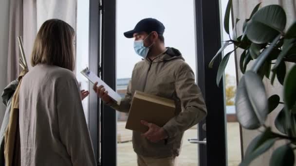 Delivery man σε μάσκα με κουτί και πελάτη στο σπίτι — Αρχείο Βίντεο