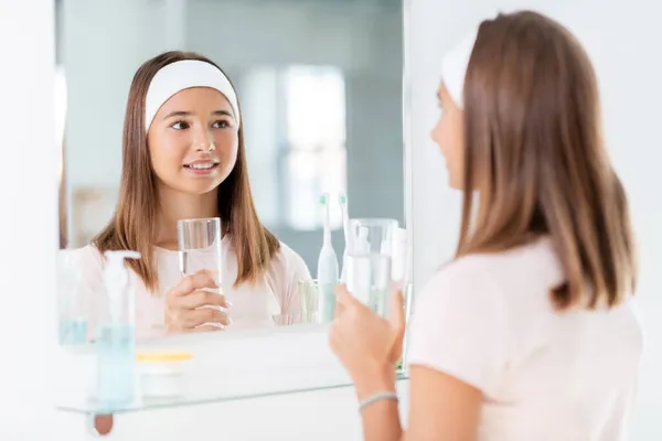 Adolescente con un bicchiere d'acqua guardando nello specchio — Foto Stock