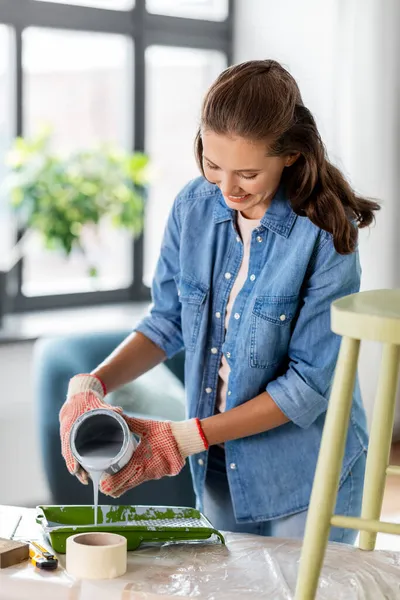 Mujer feliz verter pintura gris para bandeja en casa —  Fotos de Stock
