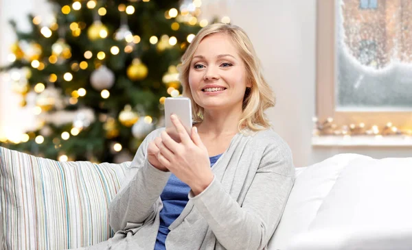 Leende kvinna med smartphone hemma på jul — Stockfoto