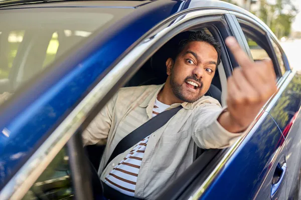 Vihainen mies ajaa autoa ja näyttää keskisormea — kuvapankkivalokuva
