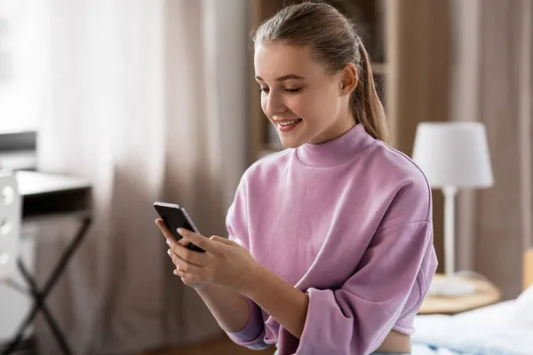 Menina sorridente com smartphone em casa — Fotografia de Stock