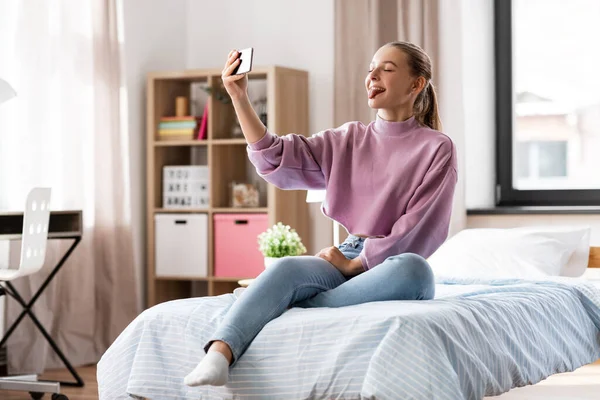 Щаслива дівчина зі смартфоном, що приймає селфі вдома — стокове фото